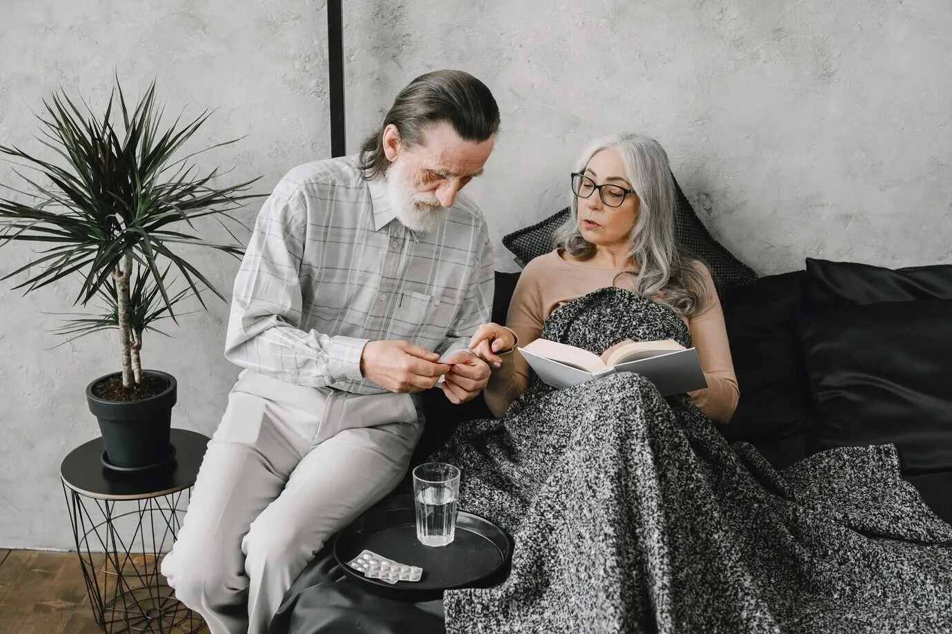 Seniorin liegt im Bett und nimmt Tabletten; ihr fürsorglicher Ehemann ist bei ihr. Krankheit, Quarantäne.